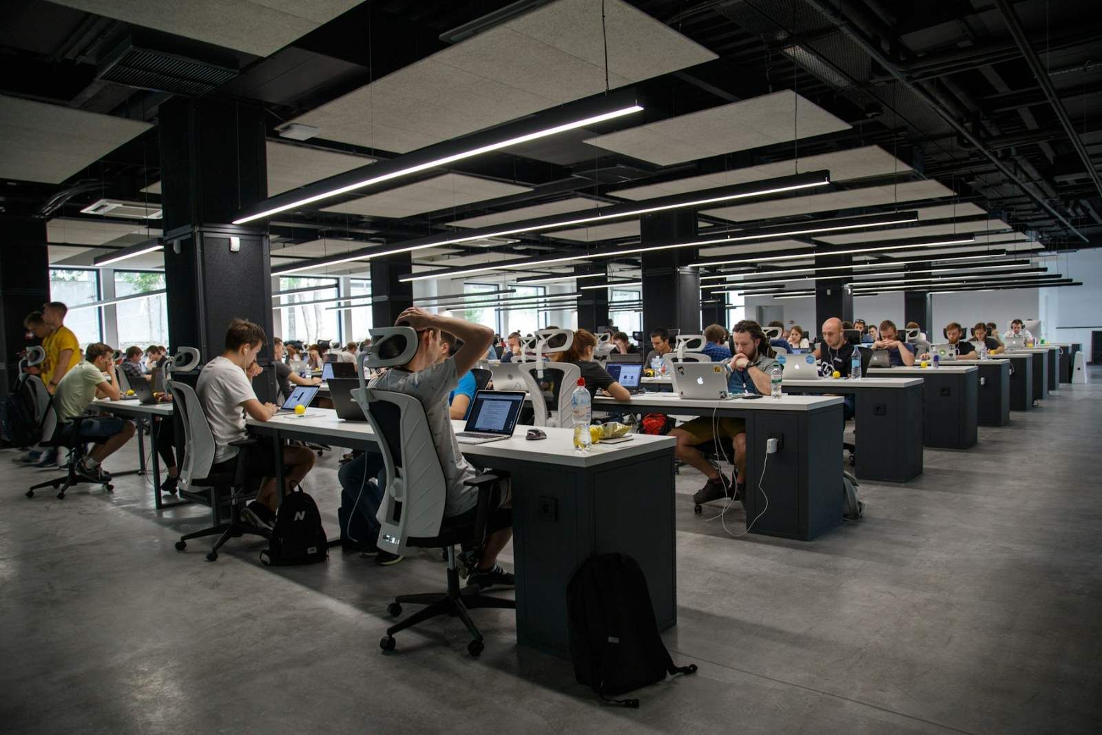 Açık planlı modern bir ofiste bilgisayar başında çalışan tasarım ve yazılım ekibi